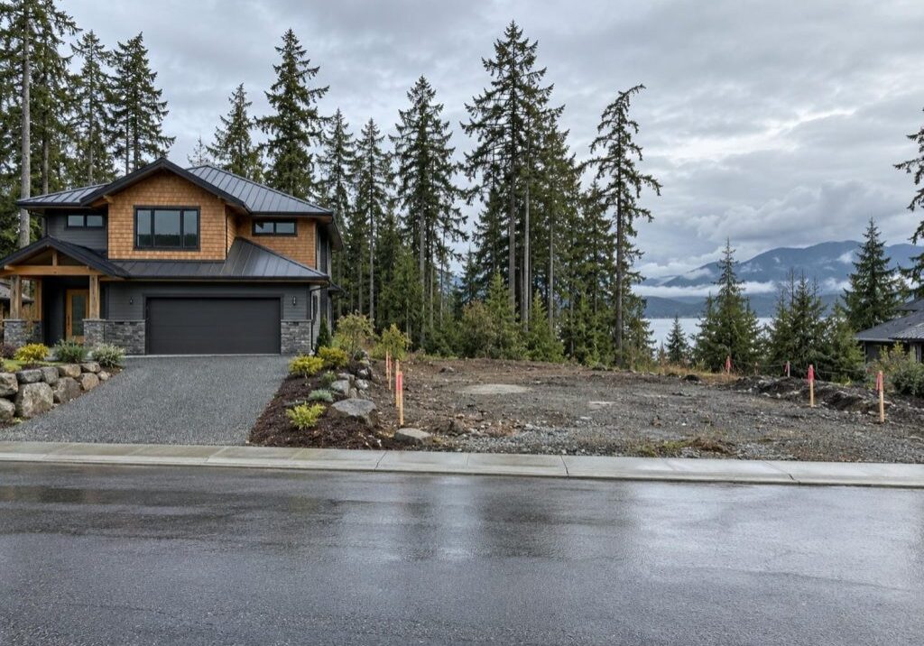 A newly finished house on a quiet street beside a cleared building lot marked with survey stakes